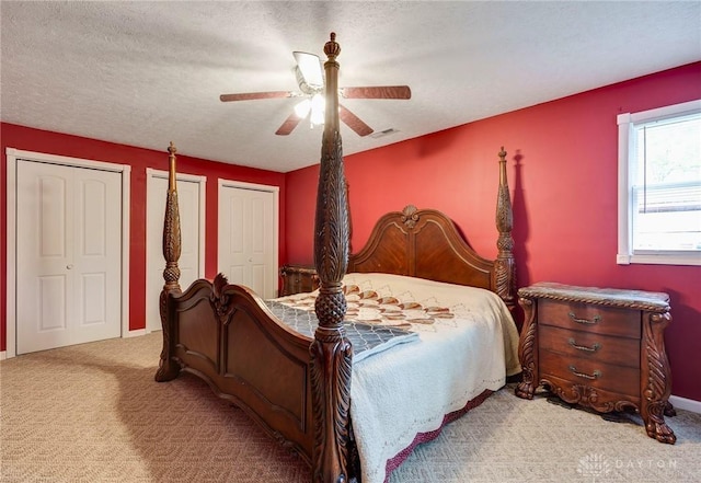 bedroom featuring a textured ceiling, two closets, ceiling fan, and light carpet