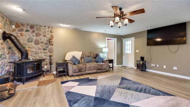 living room featuring a textured ceiling, ceiling fan, light hardwood / wood-style flooring, and a wood stove