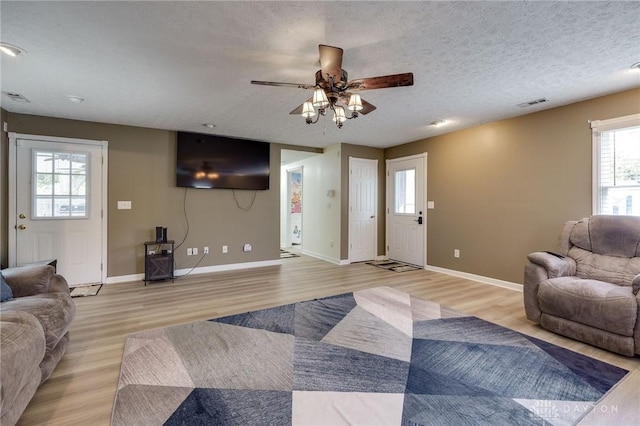 living room with ceiling fan, a textured ceiling, light wood-type flooring, and a wealth of natural light