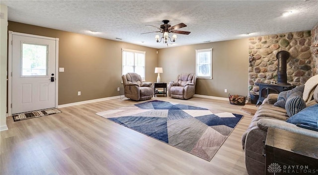 living room with a textured ceiling, ceiling fan, a wealth of natural light, and a wood stove