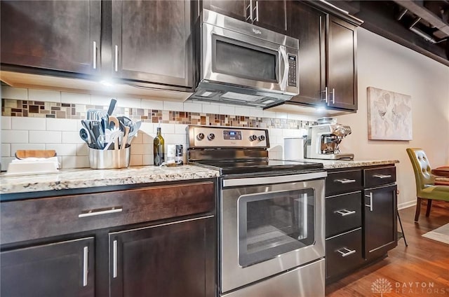 kitchen featuring light stone counters, stainless steel appliances, decorative backsplash, hardwood / wood-style floors, and dark brown cabinetry