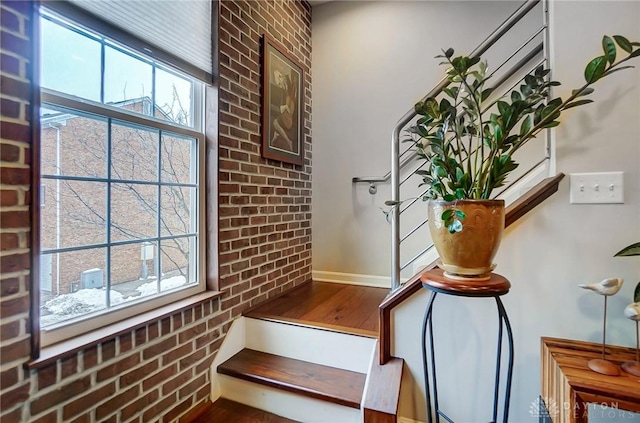 stairway with brick wall and hardwood / wood-style flooring