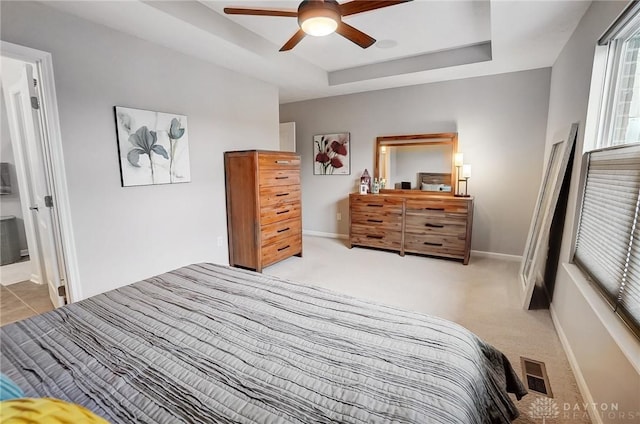 bedroom with ensuite bath, a raised ceiling, ceiling fan, and light carpet