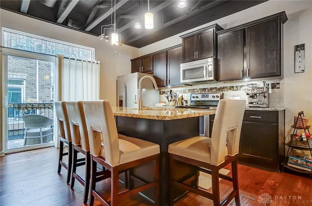 kitchen featuring appliances with stainless steel finishes, hanging light fixtures, dark wood-type flooring, light stone counters, and backsplash