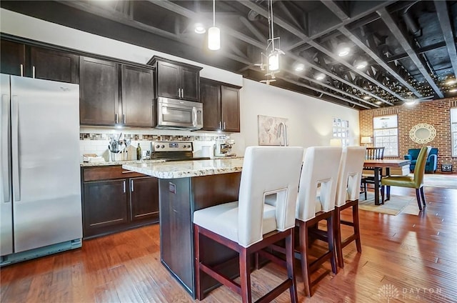 kitchen with stainless steel appliances, hanging light fixtures, brick wall, light stone counters, and decorative backsplash