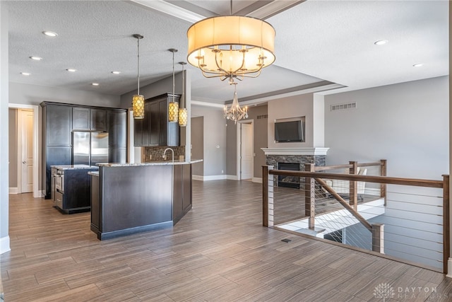 kitchen with a fireplace, an inviting chandelier, pendant lighting, and dark brown cabinetry