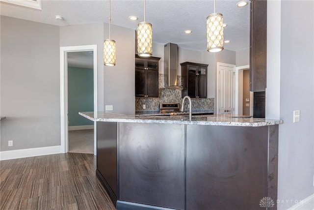 kitchen featuring kitchen peninsula, a textured ceiling, wall chimney exhaust hood, decorative light fixtures, and dark brown cabinetry