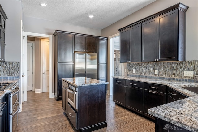 kitchen featuring stainless steel appliances, light stone countertops, a kitchen island, a textured ceiling, and tasteful backsplash