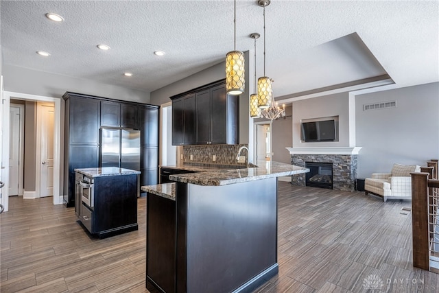 kitchen with decorative light fixtures, dark stone countertops, tasteful backsplash, a kitchen island, and a stone fireplace