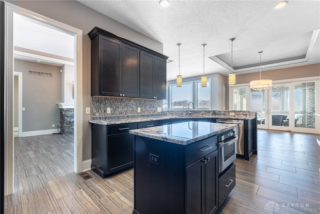 kitchen featuring sink, decorative light fixtures, stainless steel oven, tasteful backsplash, and a kitchen island