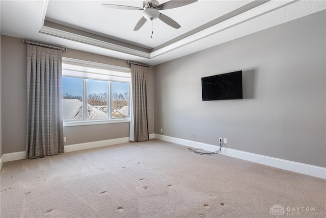 carpeted empty room with a raised ceiling and ceiling fan