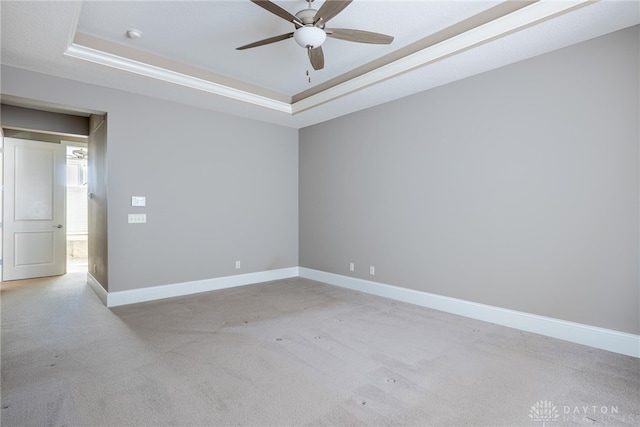 empty room with a raised ceiling, ceiling fan, and light colored carpet