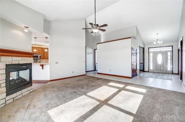 unfurnished living room featuring ceiling fan with notable chandelier, light colored carpet, a fireplace, and high vaulted ceiling