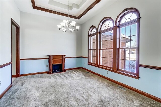 empty room with a tray ceiling, a healthy amount of sunlight, a notable chandelier, and carpet flooring