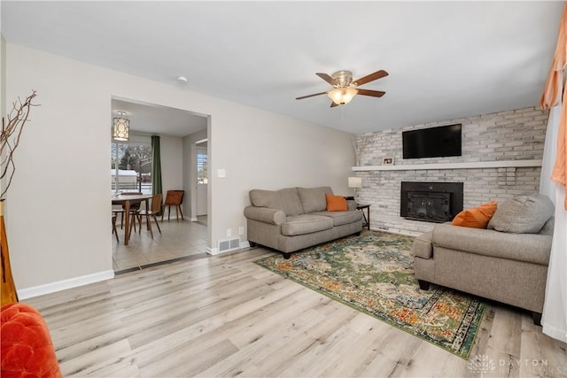 living room featuring a fireplace, ceiling fan, and light wood-type flooring