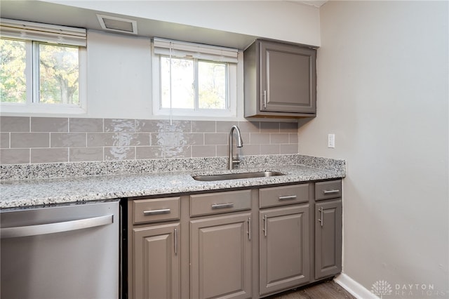 kitchen featuring tasteful backsplash, a healthy amount of sunlight, gray cabinetry, stainless steel dishwasher, and a sink