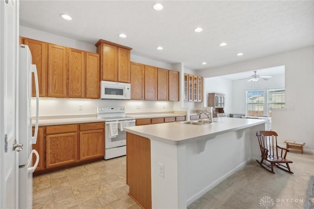 kitchen featuring white appliances, a kitchen bar, a kitchen island with sink, ceiling fan, and sink