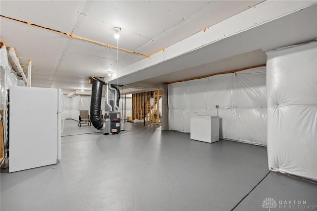 basement with white fridge, fridge, and heating unit