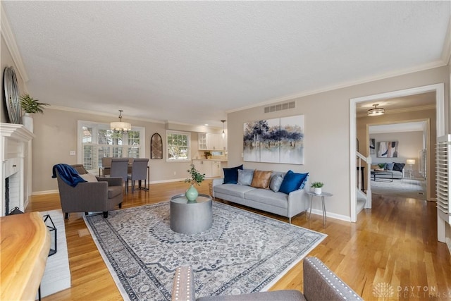 living room with a fireplace, ornamental molding, a textured ceiling, and light hardwood / wood-style flooring