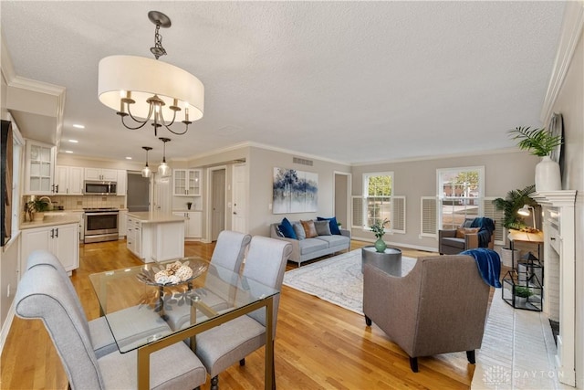 dining space featuring a textured ceiling, light wood-type flooring, an inviting chandelier, and crown molding