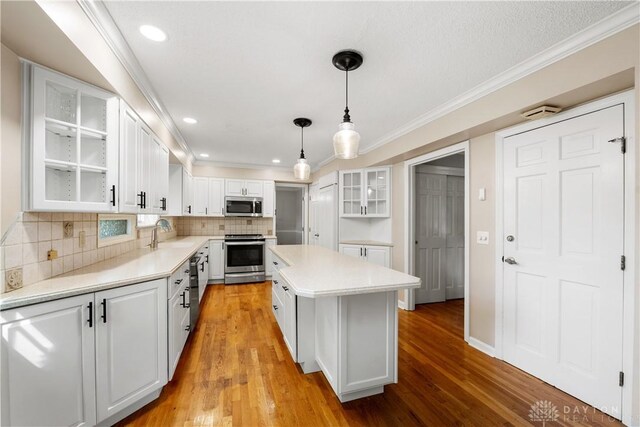 kitchen with decorative light fixtures, stainless steel appliances, decorative backsplash, light wood-type flooring, and white cabinetry