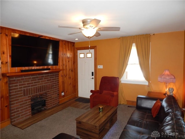 carpeted living room featuring ceiling fan, wood walls, and a fireplace