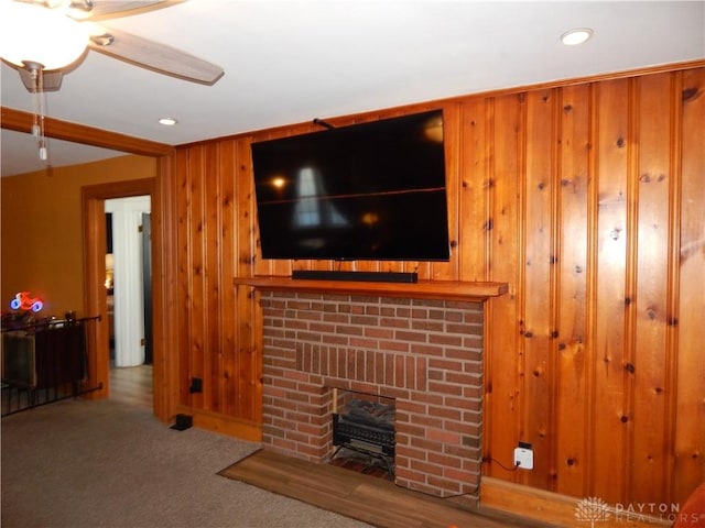 carpeted living room with a fireplace and wood walls