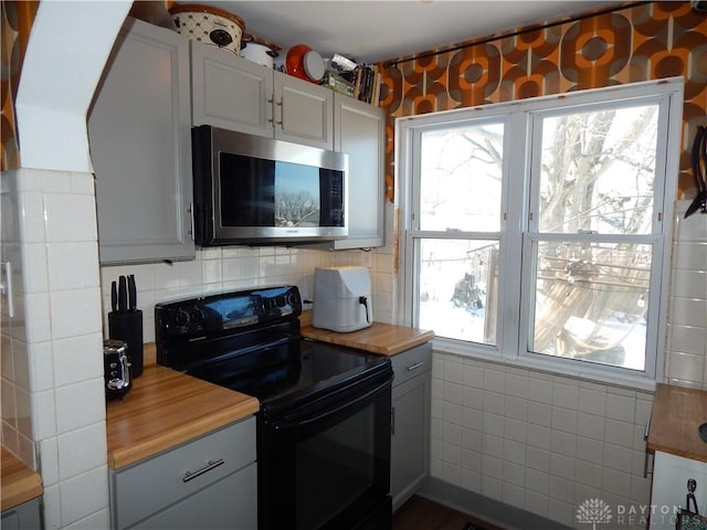 kitchen featuring backsplash, butcher block counters, black electric range, and plenty of natural light