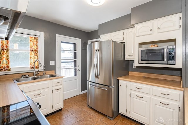 kitchen with appliances with stainless steel finishes, plenty of natural light, white cabinets, light tile patterned flooring, and sink