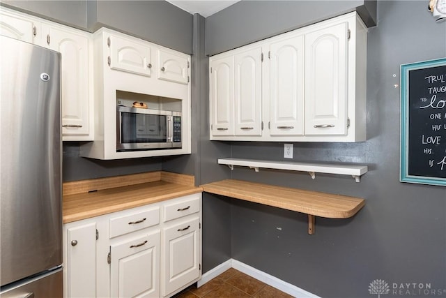 kitchen with stainless steel appliances, dark tile patterned floors, and white cabinetry