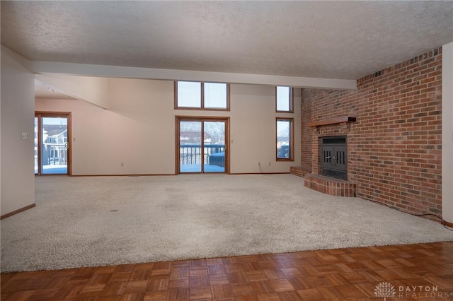 unfurnished living room featuring a fireplace, a textured ceiling, carpet, beamed ceiling, and brick wall