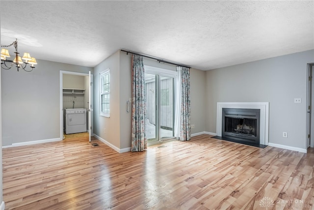 unfurnished living room with a textured ceiling, washer and dryer, light wood-type flooring, and a chandelier