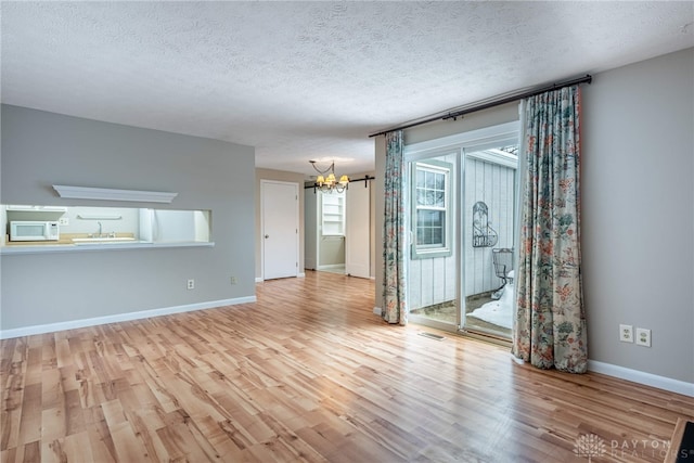 unfurnished room featuring a textured ceiling, light hardwood / wood-style floors, and a chandelier