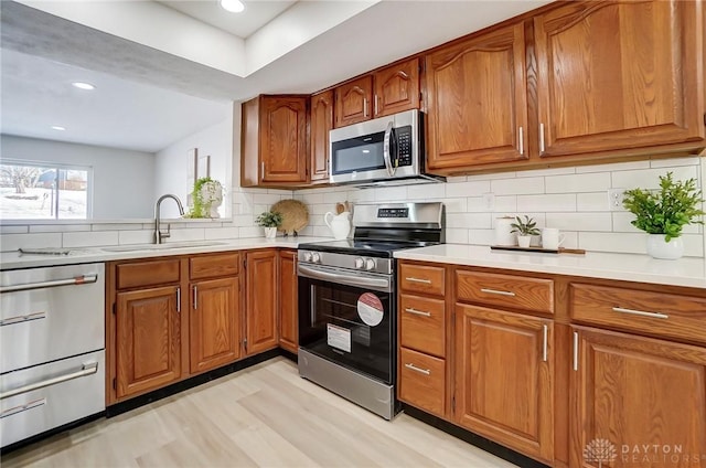 kitchen with sink, decorative backsplash, light hardwood / wood-style floors, and appliances with stainless steel finishes