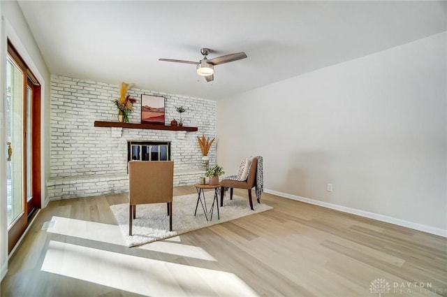 unfurnished room featuring a brick fireplace, light wood-type flooring, and ceiling fan