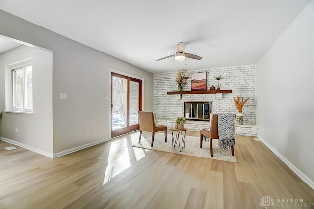 living area with a fireplace, ceiling fan, and light wood-type flooring