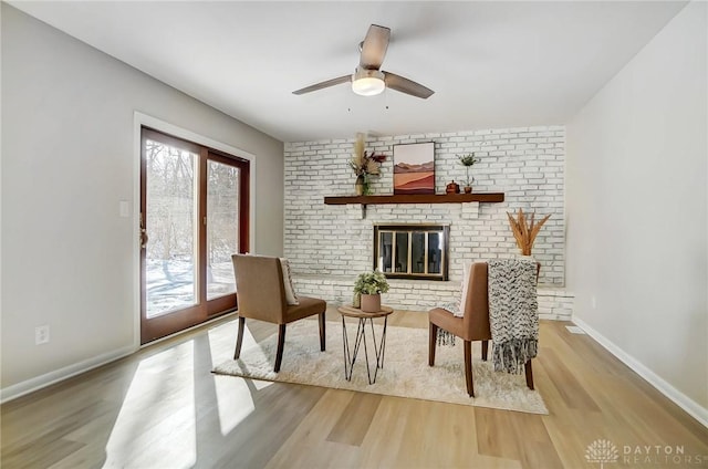 living area featuring ceiling fan, light wood-type flooring, and a fireplace