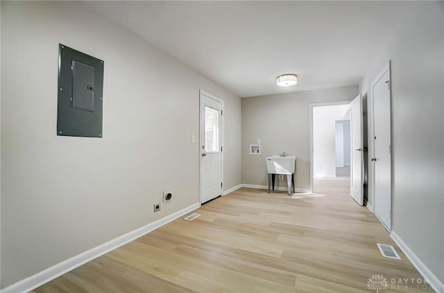 clothes washing area with electric panel, light wood-type flooring, electric dryer hookup, and washer hookup