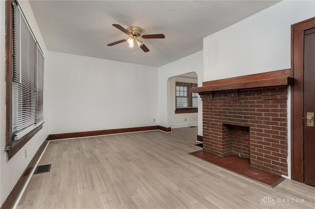 unfurnished living room with a brick fireplace, a textured ceiling, ceiling fan, and light hardwood / wood-style flooring