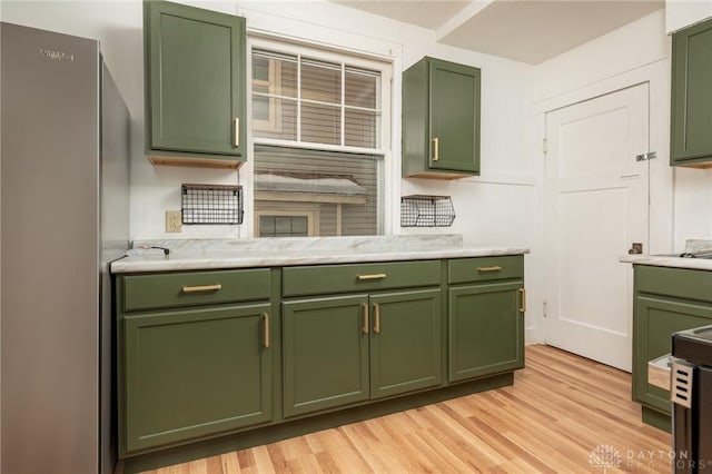 kitchen featuring stainless steel refrigerator, light hardwood / wood-style floors, green cabinets, and light stone counters