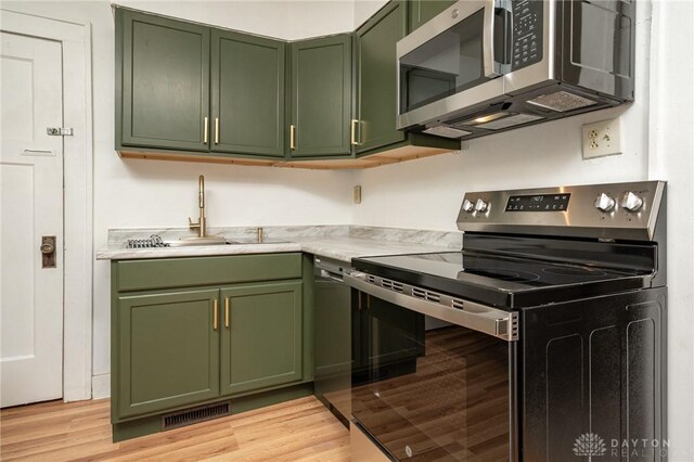 kitchen featuring stainless steel appliances, green cabinetry, light hardwood / wood-style flooring, and sink