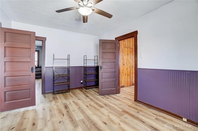 unfurnished room with ceiling fan, light wood-type flooring, and wooden walls