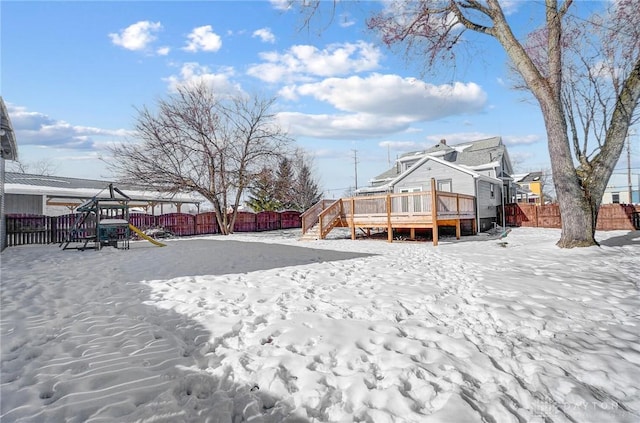 yard layered in snow featuring a playground and a wooden deck