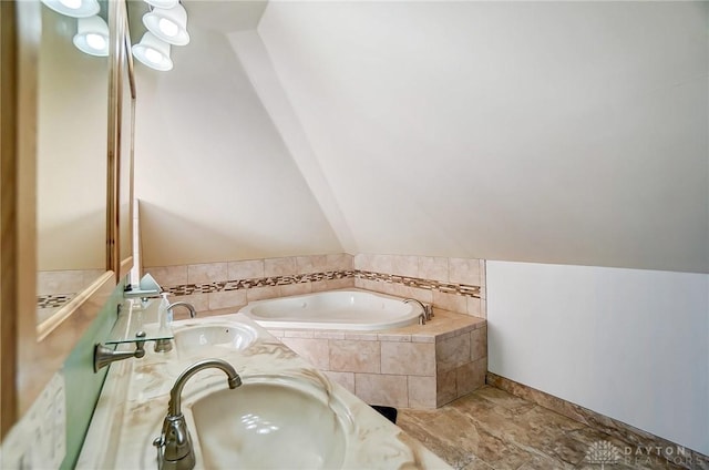 bathroom with lofted ceiling, a relaxing tiled tub, and sink