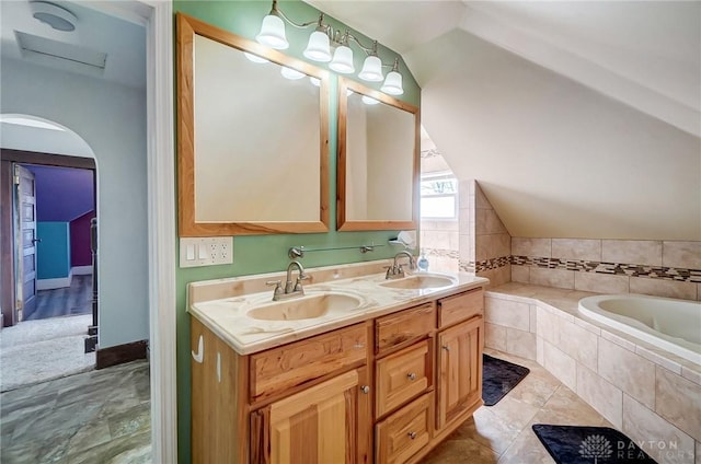 bathroom with vanity, tiled tub, and vaulted ceiling