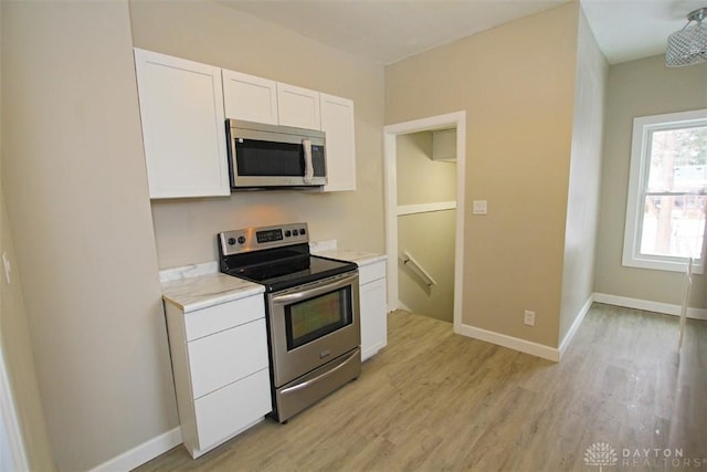 kitchen with light wood-style flooring, white cabinetry, stainless steel appliances, and baseboards