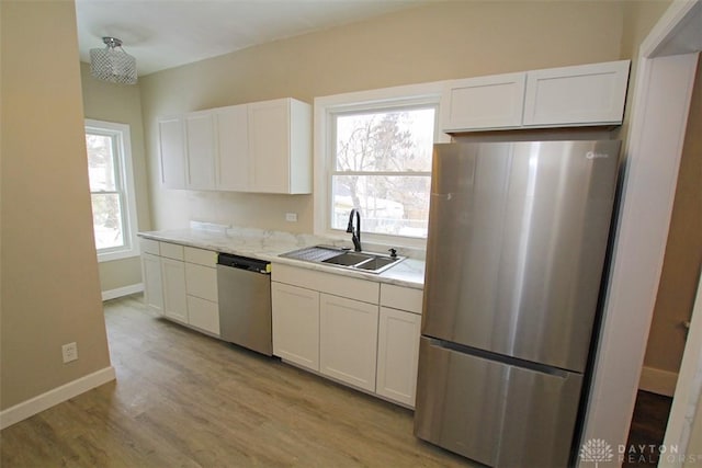 kitchen featuring stainless steel appliances, light countertops, white cabinetry, a sink, and light wood-type flooring