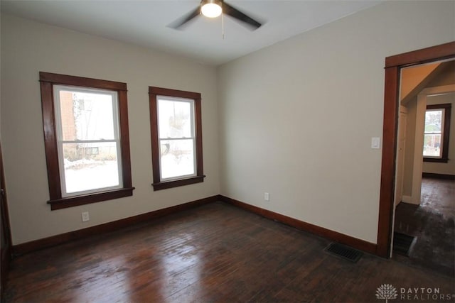 empty room with baseboards, visible vents, dark wood finished floors, and a wealth of natural light