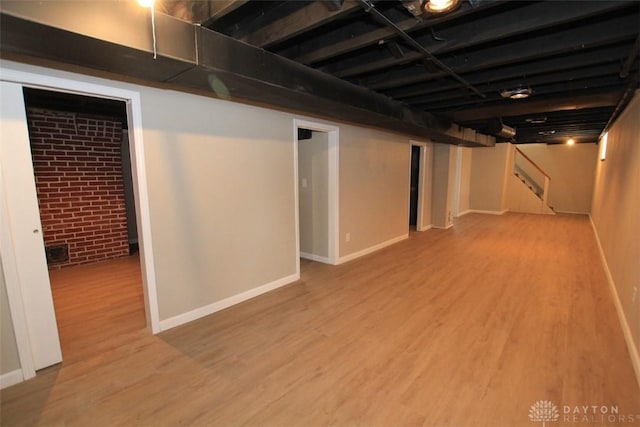 finished below grade area featuring baseboards, brick wall, stairway, and wood finished floors