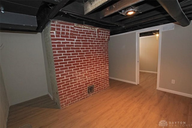 finished basement with brick wall, wood finished floors, visible vents, and baseboards